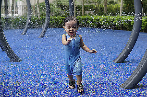 Glücklicher Junge spielt im Wasser im Park