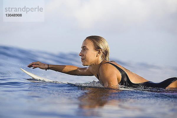 Zuversichtliche Frau liegt auf einem Surfbrett am Strand gegen den Himmel