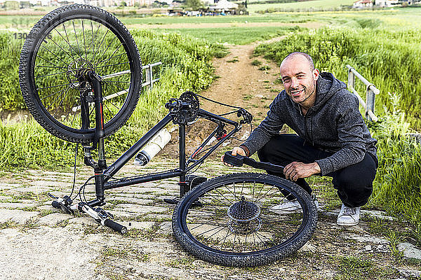 Porträt eines Mannes  der ein Fahrrad auf einem Feld repariert  gegen einen Bauernhof