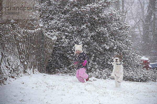 Glückliches Mädchen spielt mit Hund auf dem Feld bei Schneefall