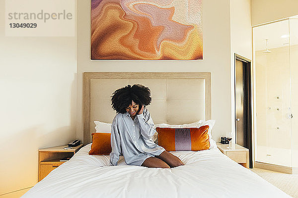Lächelnde Geschäftsfrau sitzt im Hotelzimmer auf dem Bett