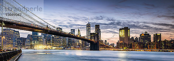 Brooklyn Bridge über den East River in der Stadt gegen bewölkten Himmel in der Abenddämmerung