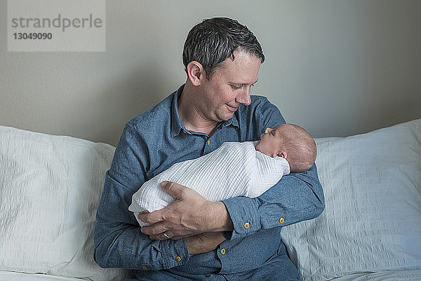Vater trägt neugeborenen Jungen  während er zu Hause auf dem Sofa sitzt