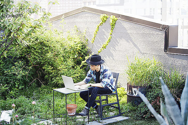 Mann benutzt Laptop  während er auf der Terrasse sitzt