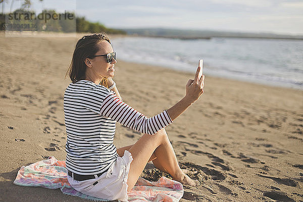 Frau mit Sonnenbrille  die beim Entspannen am Strand Selfie nimmt