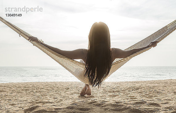 Rückansicht einer Frau  die sich auf einer Hängematte am Strand entspannt