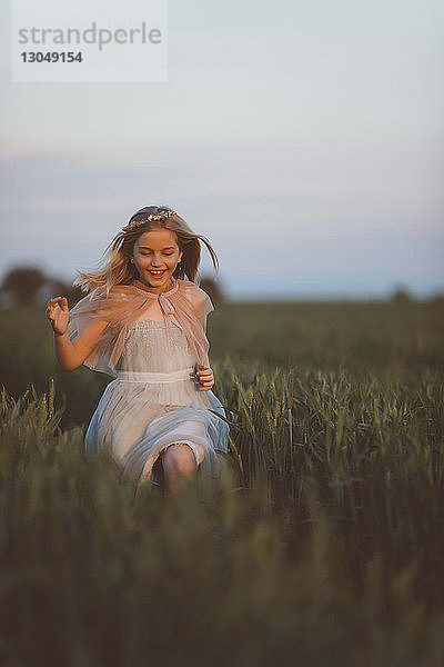 Fröhliches Mädchen rennt bei Sonnenuntergang auf Grasfeld gegen den Himmel
