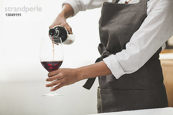 Mittelteil einer Frau  die Rotwein in ein Glas einschenkt