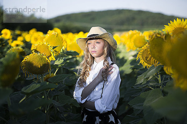 Nachdenkliches Teenager-Mädchen mit Cowboyhut steht im Sonnenblumenfeld