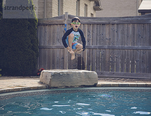 Unbeschwerter Junge springt gegen Zaun in Schwimmbad