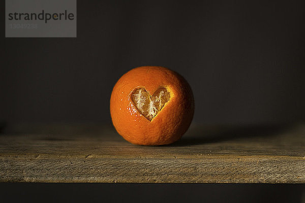 Nahaufnahme eines herzförmigen Musters in Orangenschale auf einem Holztisch