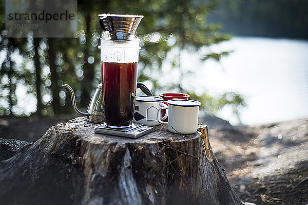 Nahaufnahme von Kaffeetassen und Wasserkocher am Baumstumpf auf dem Campingplatz