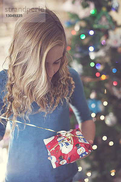 Mädchen öffnet Weihnachtsgeschenk im Stehen zu Hause