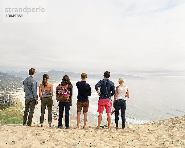 Rückansicht von Freunden  die auf Sand am Strand gegen den Himmel stehen