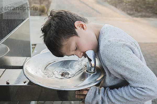 Durstiger Junge trinkt Wasser aus Brunnen im Park