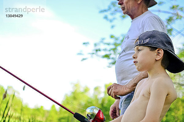 Seitenansicht eines Jungen mit Großvater  der gegen den Himmel fischt