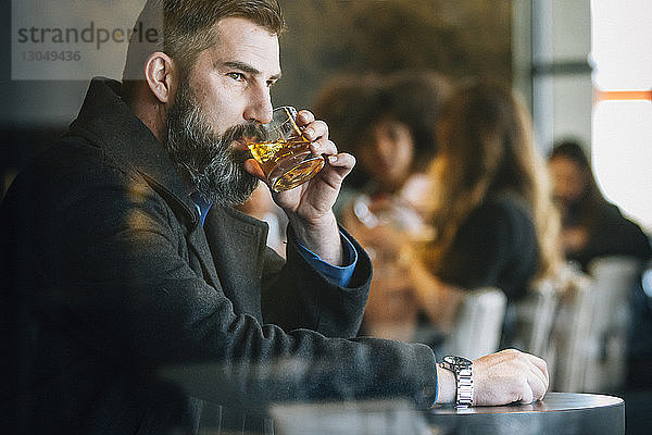 Nachdenklicher Geschäftsmann trinkt Alkohol im Hotel durch Fenster gesehen