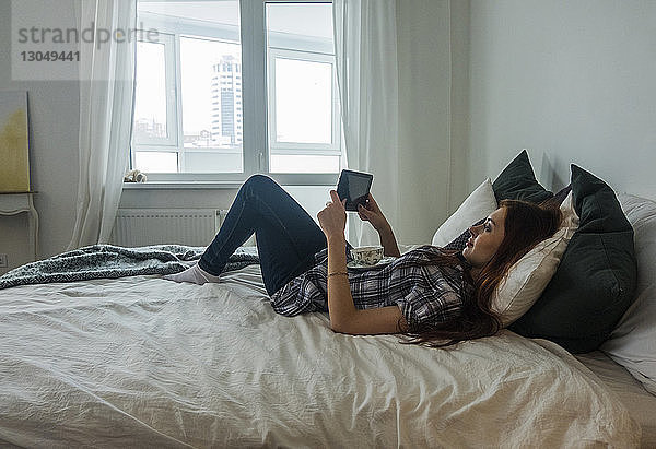 Teenager-Mädchen liegt im Bett  während sie zu Hause einen Tablet-Computer benutzt