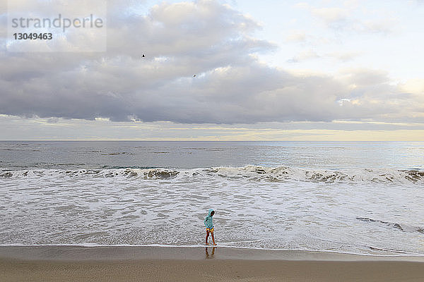 Mädchen geht am Laguna Beach gegen bewölkten Himmel
