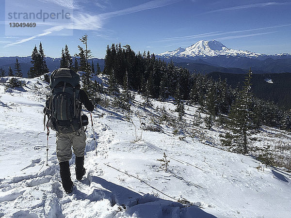 Rückansicht eines Mannes mit Rucksack und Skistöcken beim Gehen auf schneebedecktem Feld