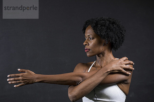 Selbstbewusste Frau streckt die Arme aus  während sie im Fitnessstudio an der Wand steht