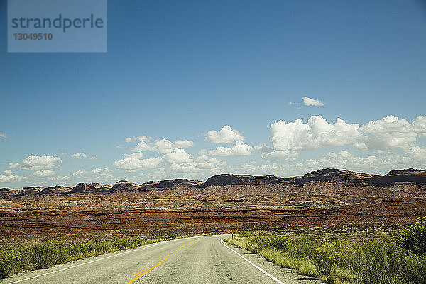 Leere Straße inmitten der Landschaft gegen blauen Himmel bei sonnigem Wetter