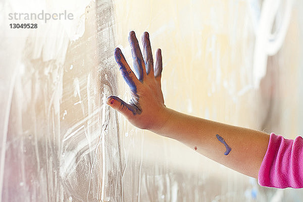 Geschnittene Hand eines Mädchens mit Farbe berührt Fenster zu Hause