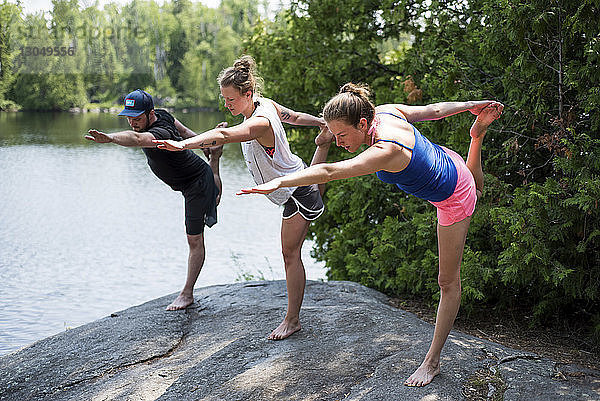 Freunde strecken die Beine beim Yoga-Üben auf einem Felsen am Seeufer