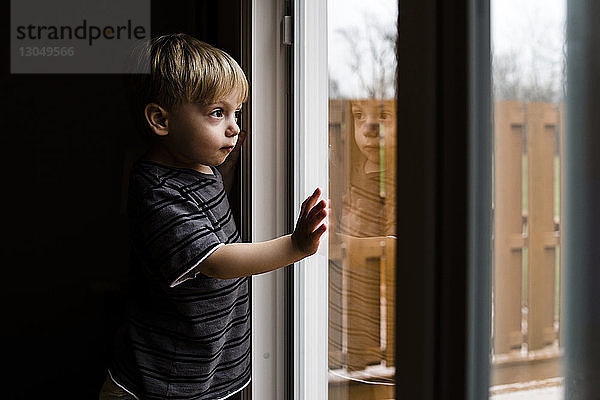 Seitenansicht eines nachdenklichen Jungen  der durch ein Fenster schaut