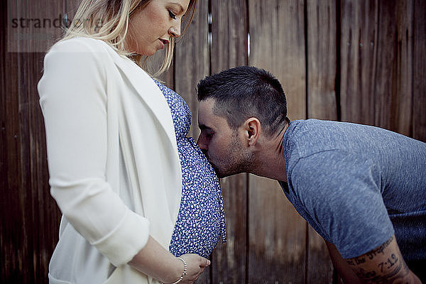 Mann küsst auf den Bauch einer schwangeren Frau