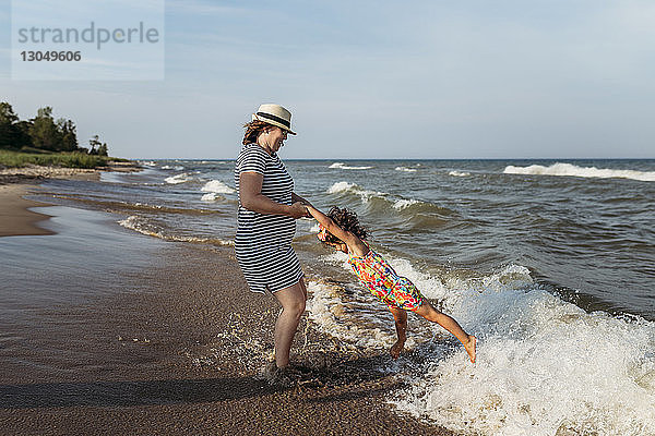 Verspielte Mutter dreht Tochter am Strand gegen den Himmel