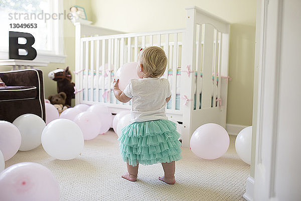 Rückansicht eines kleinen Mädchens  das zu Hause mit Luftballons spielt