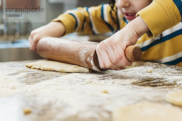 Mittelteil eines Jungen  der zu Hause in der Küche Teig rollt