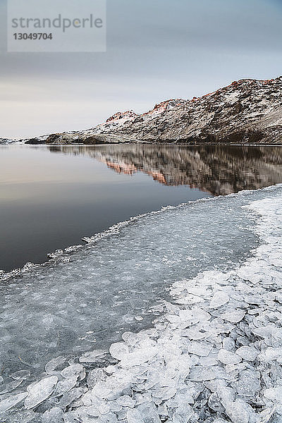 Szenische Ansicht eines Sees an Bergen mit Eis im Vordergrund