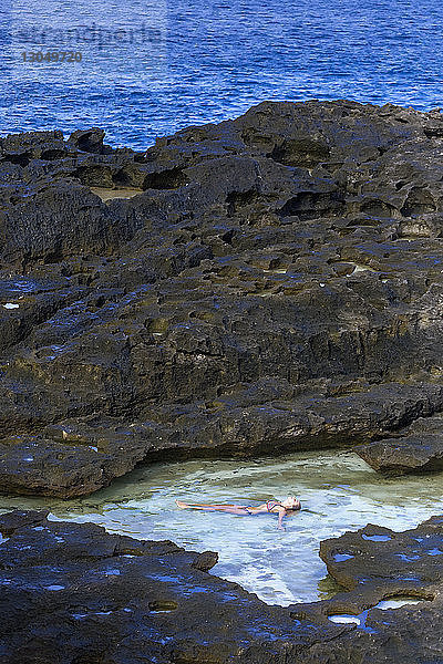 Hochwinkelaufnahme einer Bikini tragenden Frau  die an Felsen im Meer liegt