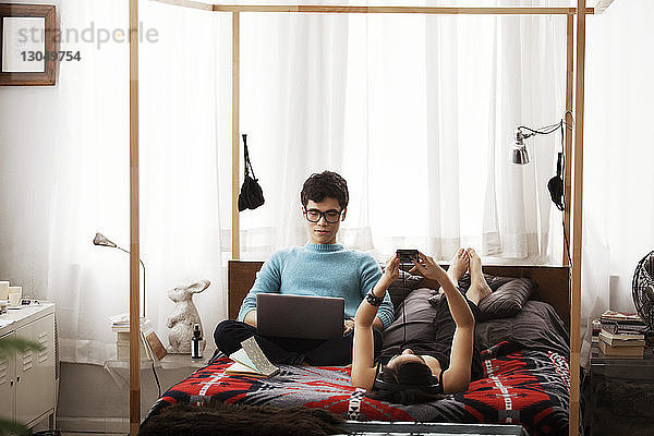 Paar benutzt zu Hause am Bett Laptop und Smartphone