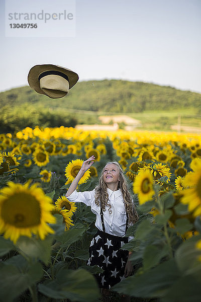 Glückliche Teenagerin wirft Cowboyhut auf Sonnenblumenfeld