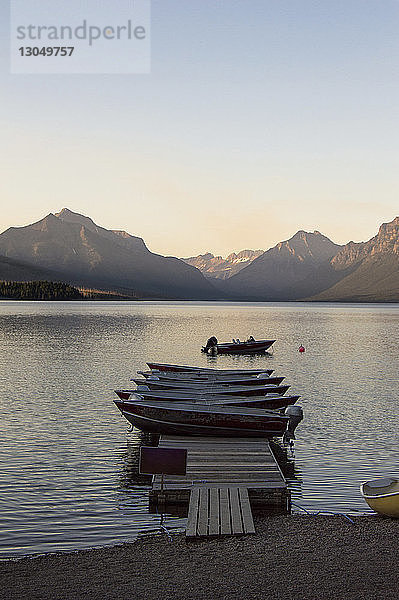 Boote vertäut an der Mole auf dem See vor klarem Himmel im Glacier National Park bei Sonnenuntergang