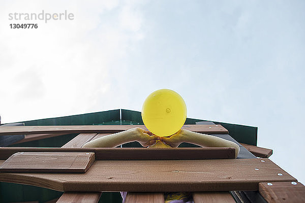 Niedrigwinkelansicht eines Mädchens  das einen Ballon bläst  während es in einem Spielgerät im Freien gegen den Himmel steht