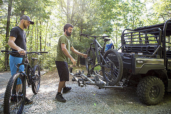 Mann sieht Freund an  der im Wald ein Mountainbike auf ein Geländefahrzeug setzt