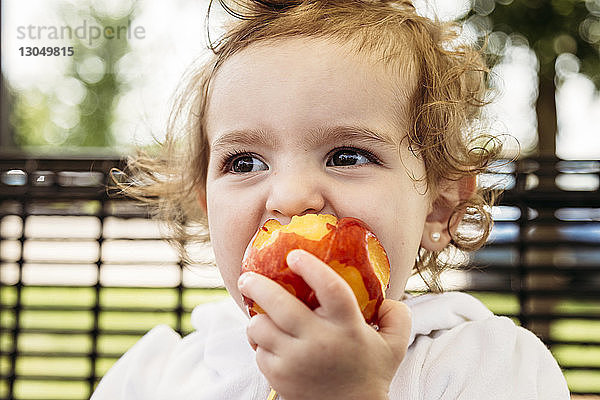 Süßes Mädchen schaut weg  während sie im Hof einen Apfel isst