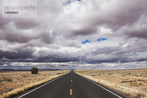 Leere Straße mitten auf dem Feld gegen stürmische Wolken