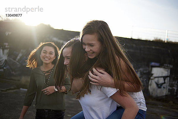 Glückliche Teenagerin schaut Freunden bei Sonnenschein huckepack zu