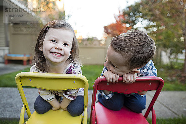 Nahaufnahme von lächelnden Geschwistern  die auf Stühlen im Hof knien