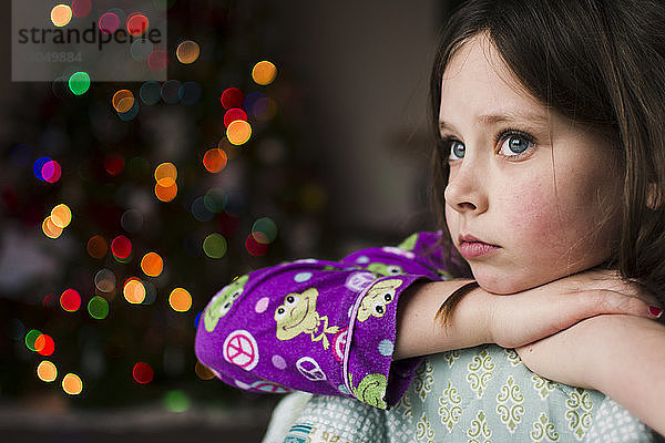 Nachdenkliches Mädchen gegen erleuchteten Weihnachtsbaum zu Hause