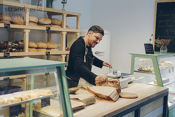 Glücklicher Besitzer hält Papiertüte in der Hand  während er am Tresen in einer Bäckerei steht