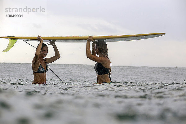 Freunde tragen während der Regenzeit Surfbrett auf dem Kopf im Meer