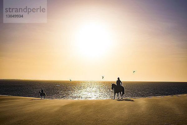 Silhouette von Menschen  die am Strand am Strand gegen den Himmel reiten