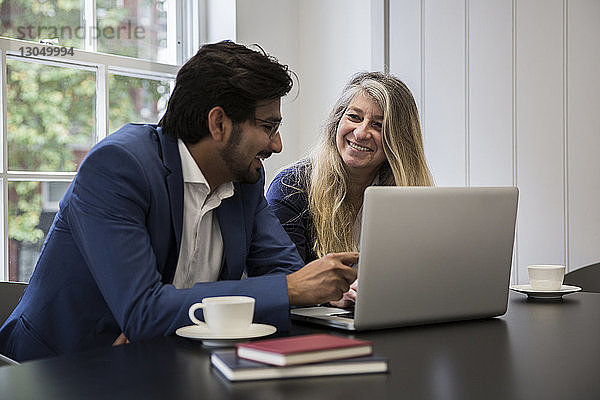 Lächelnde Geschäftsleute diskutieren über Laptop-Computer am Schreibtisch im Büro