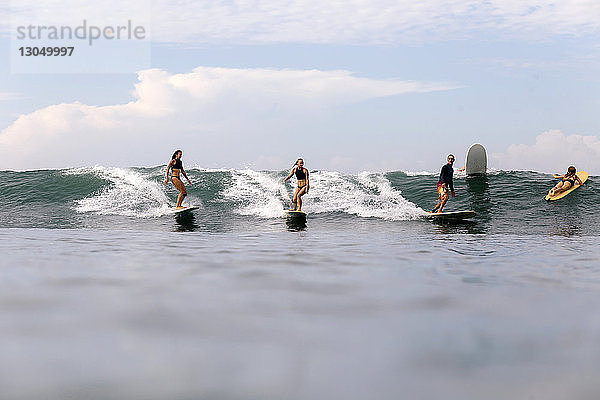 Freunde surfen auf dem Meer gegen den Himmel